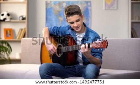 Cheerful Caucasian teenager playing guitar, enjoying favorite hobby, leisure