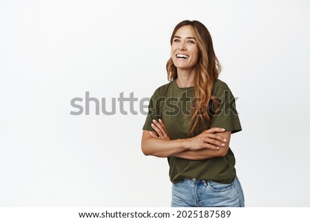 Cheerful caucasian woman cross arms on chest, laughing and smiling white teeth, looking aside left at promo text, posing with cheerful face expression, studio background