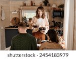 Cheerful Caucasian woman setting table with tea and muffins for family meal with her husband and daughter in wooden country house