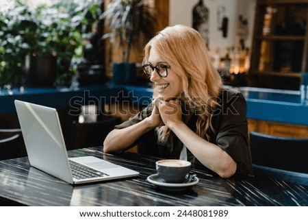 Cheerful caucasian young businesswoman freelancer watching movies films webinars working on distance remotely on laptop in cafe restaurant