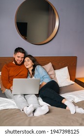 Cheerful Caucasian Young Couple Watching Video Online On Laptop Lying In Bed At Night, Cuddling And Watching Movie On Computer. Concept Of Leisure Activity Of Lovers At Home.