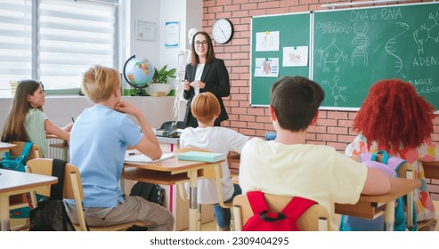 Cheerful Caucasian young female teacher of anatomy or biology talking to class and explaining human DNA to pupils. At school. Education concept. Indoors. Teaching. Lection about body. - Powered by Shutterstock