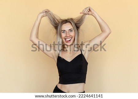 Cheerful caucasian young woman grimacing, fooling and making funny faces during photoshoot. Studio shot of pretty girl fooling around on beige background. Humor concept