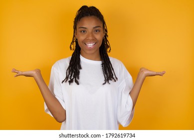 Cheerful cheery optimistic Young dark skinned woman with braids hair wearing casual clothes girl holding two palms copy space