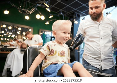 Cheerful child in barbershop chair at the end of haircut, barber using hairdryer to remove loose hair clippings. Enjoyment or satisfaction with the haircut experience. - Powered by Shutterstock