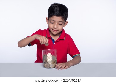 Cheerful child boy putting coins in a glass jar. Concept of saving. Child saving money. Royalty free image of a cute boy collecting coins in a glass jar for toys - isolated on white background