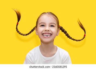 Cheerful child girl with growing teeth throws pigtails and laughs on a yellow background. Funny girl has fun and shows positive emotions by playing with her hair. Happy childhood concept