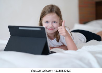 Cheerful Child Girl Showing Thumb Up Lying On Bed With Tablet