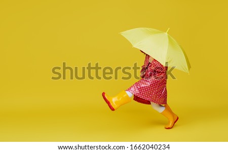 Cheerful child girl with yellow umbrella and red rain coat on colored yellow background. Copy space for text