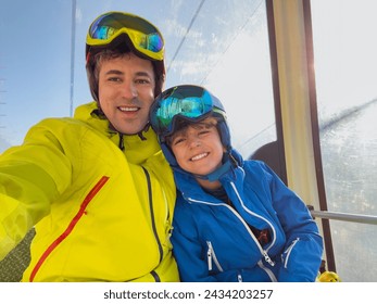 Cheerful child with his father wearing ski gear enjoy a ride on a cable car do selfies against the sunny picturesque landscape of snowy mountains - Powered by Shutterstock