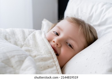 Cheerful Child Looking At Camera While Lying In Bed Under White Blanket