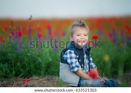 Cheerful child, smiling and laughing in a large field of flowering poppies, in a straw hat and shirt