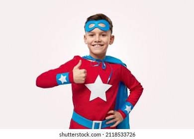 Cheerful child in superhero costume showing like gesture and looking at camera on white background in studio - Powered by Shutterstock