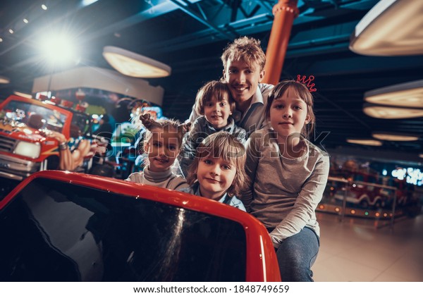 Cheerful children with dad in the entertainment center\
are having fun. Dad with children sitting in a toy car and looking\
at the camera. 