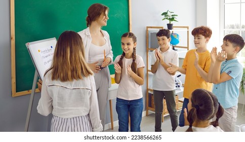 Cheerful children teens and woman teacher applauding female classmate who wrote correct solution on flipchart standing in bright classroom of modern school. Primary education, back to school