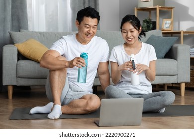 Cheerful Chinese Middle Aged Man And Young Woman In Sportswear Sitting On Fitness Mat, Drinking Water After Workout At Home, Looking At Computer Screen And Smiling, Copy Space