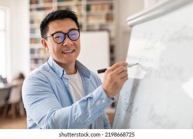 Cheerful Chinese Tutor Smiling To Camera Teaching English Language Writing Grammar Rules On Whiteboard Standing In Classroom Indoor. Modern School Education Concept