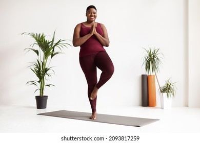 Cheerful Chubby Young Black Woman Doing Yoga At Fitness Studio, Standing In Tree Position On Yoga Mat, Smiling At Camera, Enjoying Daily Practice, Copy Space, Full Length Shot