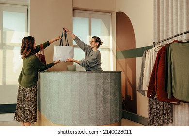 Cheerful clothing store owner handing a female customer a shopping bag with her clothing items. Happy small business owner assisting an online shopper during an in store collection.
