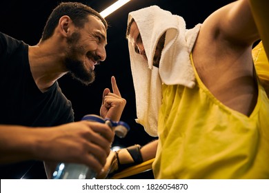 Cheerful coach sticking his finger up while instructing a fighter with a white towel on his head - Powered by Shutterstock