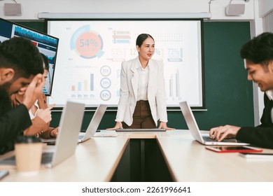 A cheerful and confident Asian businesswoman stands, present bar charts data from projector screen to her office colleagues. Asian business women leader role at the meeting.