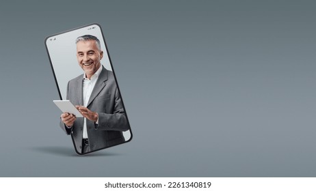 Cheerful confident businessman holding a digital tablet  in a smartphone videocall and smiling, online  service concept - Powered by Shutterstock