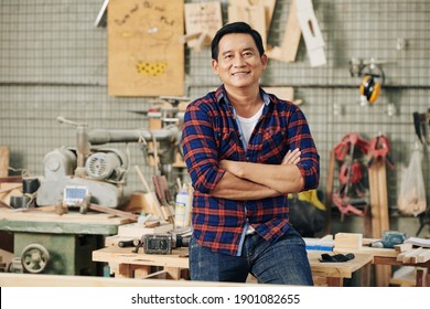 Cheerful confident carpenter in plaid shirt standing in his carpentry workshop with arms folded - Powered by Shutterstock