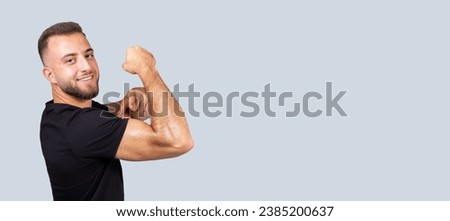Cheerful confident strong millennial european man with beard in sportswear point finger at muscle biceps on hand, isolated on gray background. Body care, sport lifestyle and workout recommendation