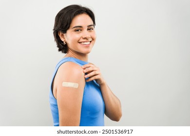 Cheerful, confident young woman grins happily after receiving a vaccination in a clinic. The bandage on her arm reflects her dedication to health and wellness - Powered by Shutterstock