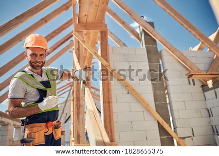 Cheerful constructor keeping smile on his face while working on top floor of house