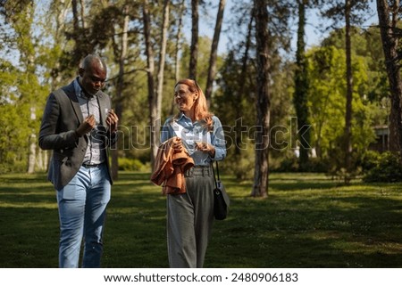 A cheerful conversation between two elegantly dressed people in a park, a middle-aged bald black man and a blonde white woman in her 30s.