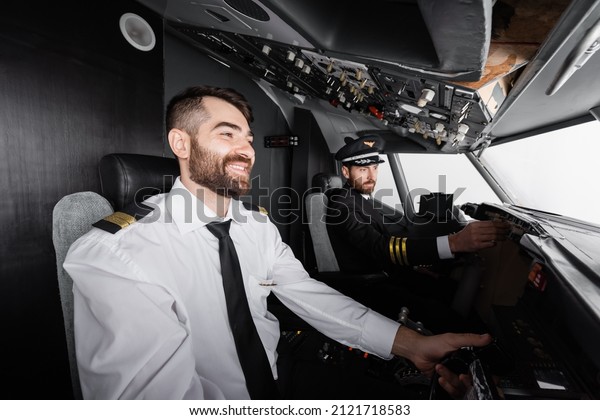 cheerful co-pilot using yoke near captain\
reaching control panel in airplane\
simulator