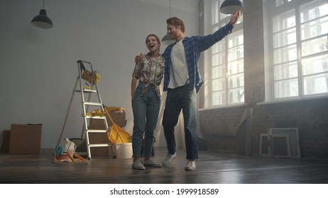 Cheerful couple admiring results of house renovation indoors. Amazed woman and man turning around in new apartment with tools for home repair. Happy family hugging indoors.