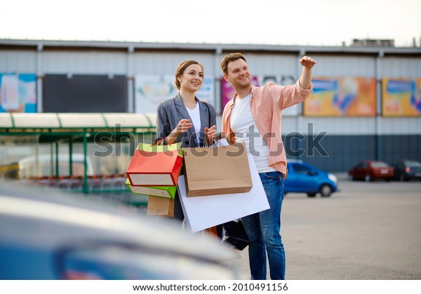 Cheerful couple\
with bags on supermarket\
parking