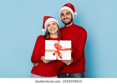 A cheerful couple, both wearing red sweaters and Santa hats, holding a beautifully wrapped gift adorned with a ribbon, embodying the joy of Christmas and togetherness. - Powered by Shutterstock