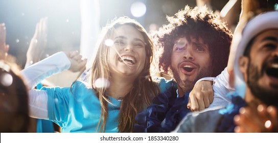 Cheerful couple cheering at a live soccer match. Group of people in the stadium cheering argentina football team.