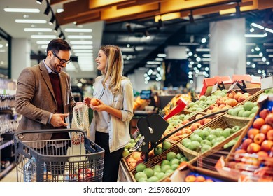 Cheerful couple choosing fruit at groceries department of the supermarket. Man holding mesh bag and woman holding fruits. Shopping at the modern mall