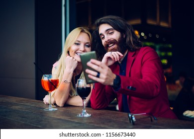 Cheerful couple drinking aperitif in a cocktail bar and having a pleasant conversation - Friends taking selfie with phone - Powered by Shutterstock