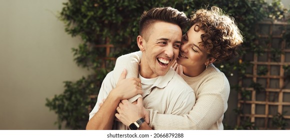 Cheerful couple embracing each other outdoors. Happy young queer couple smiling cheerfully while standing together during the day. Young LGBTQ+ couple spending quality time together.