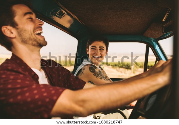 Cheerful couple enjoying a road trip.\
Smiling man and woman talking while driving in\
car.