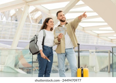 A cheerful couple is exploring the airport terminal with a map and luggage, seemingly in search of their gate, man and woman enjoying travelling together, free space