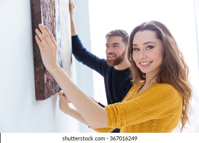 Cheerful Couple Hanging Picture On The Wall At Home