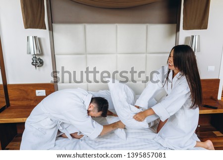 Cheerful couple have fun in the bedroom fighting with big pillows at home