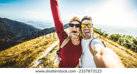 Cheerful couple of hikers taking selfie on top of the mountain - Millennial guy and girl enjoying summertime day out laughing at camera together - Millenial travelers standing on nature background