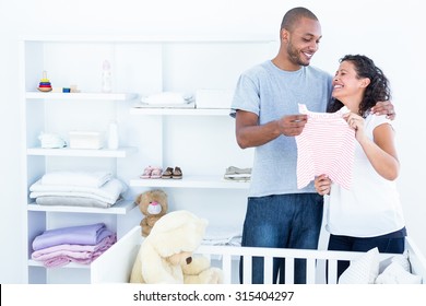 Cheerful couple holding baby clothing in bedroom at home - Powered by Shutterstock