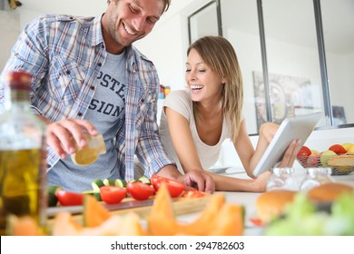 Cheerful Couple In Kitchen Cooking Dinner, Using Tablet