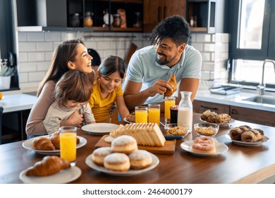 Cheerful couple laughing and embracing children during breakfast at kitchen table at home. - Powered by Shutterstock