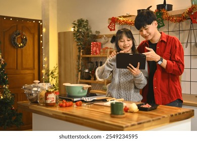 Cheerful couple looking recipe or cooking instructions on digital tablet for Christmas dinner at home - Powered by Shutterstock