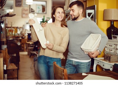 Cheerful Couple Looking For Wall Hanger In Shop Of Secondhand Furniture