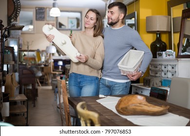 Cheerful Couple Looking For Wall Hanger In Shop Of Secondhand Furniture